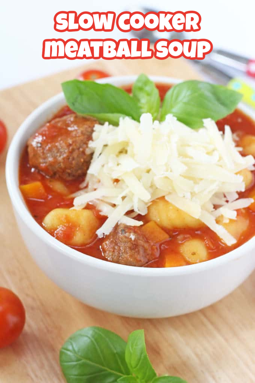 Meatball Soup served in a white bowl on a wooden chopping board and garnished with grated cheese and a sprig of fresh basil.