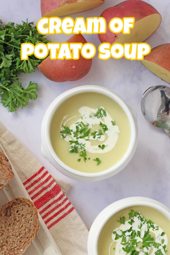 Two white bowls filled with cream of potato soup with a swirl of cream and freshly chopped herbs on top with slices of freshly cut brown bread on the side.