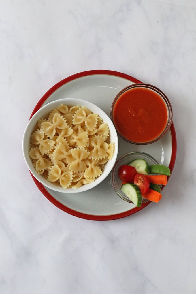 A small bowl of Hidden Veggie Tomato Sauce served separate along side a bowl of plain paste and a bowl of fresh chopped carrot,cucumber and cherry tomato's. 