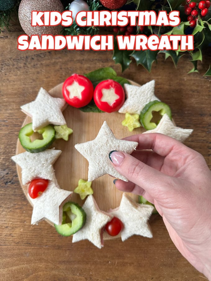Kids Christmas Sandwich Wreath  served on a wooden board with mini cheeses and cucumber with stars cut out of them.