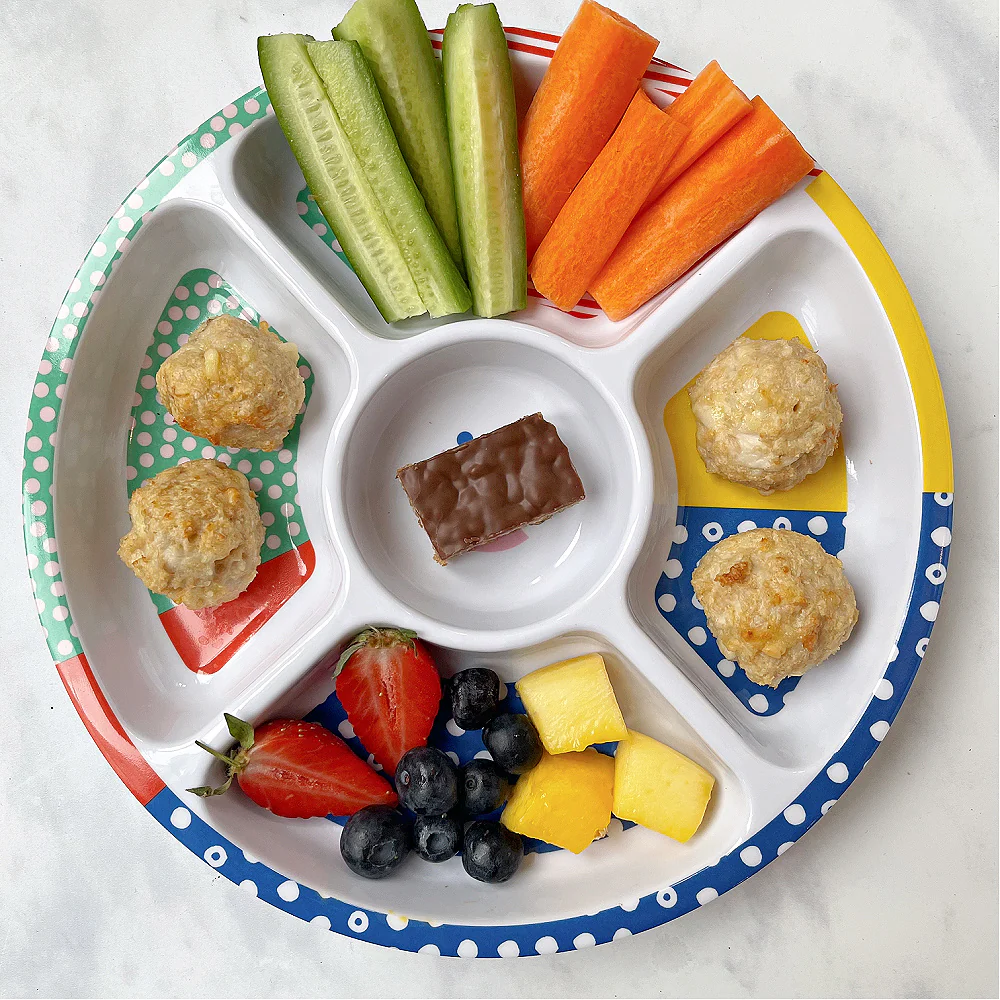 Cheesy Chicken Meatballs served in a  colourful divided kids plate from Pick Plates with chopped veggies, fruit and a chocolate flapjack.