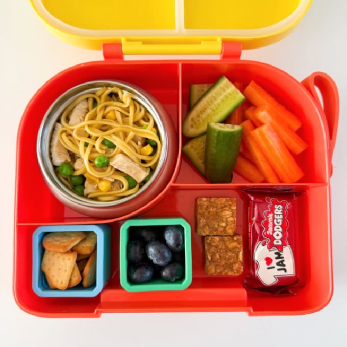 Chicken noodles served in a hot & cold lunch box with sliced carrots and cucumber.
