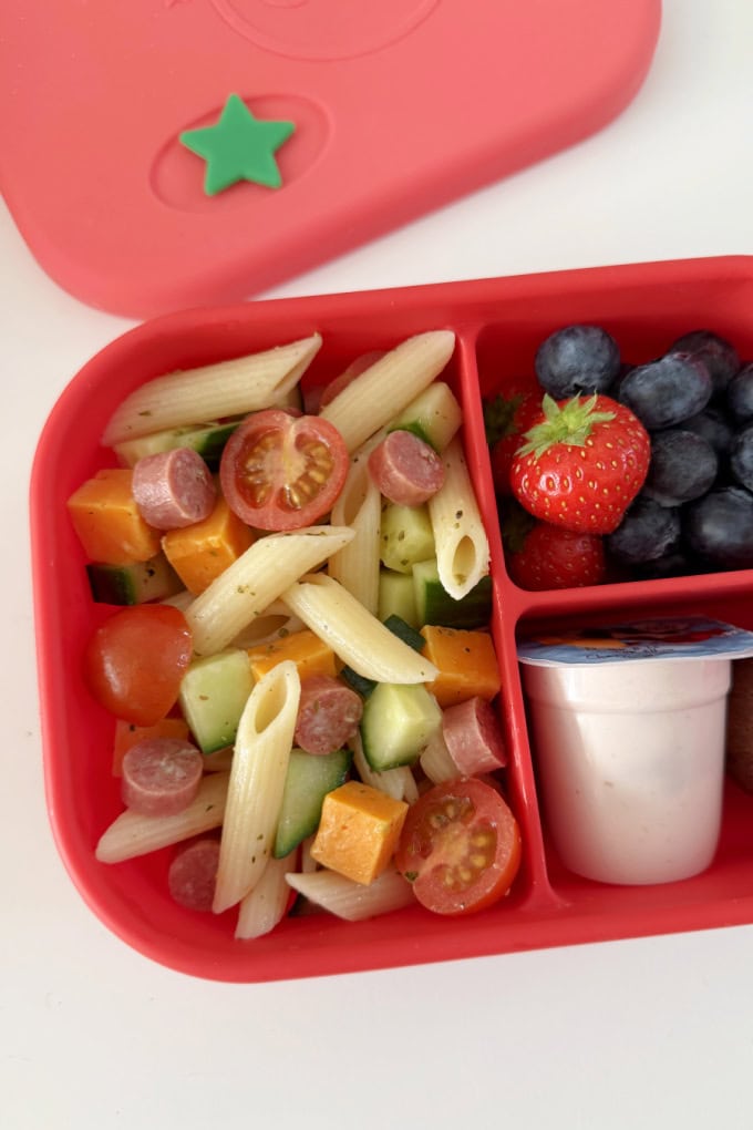 5 Minute Lunchbox Pasta Salad served in a bright red lunch box with fresh berries, yogurt and a sweet treat.