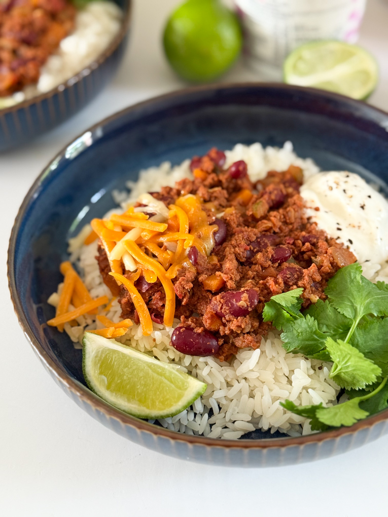 Served with white rice,grated cheese. And garnished with a slice of lime and a sprig of coriander. In a round dark blue bowl.
