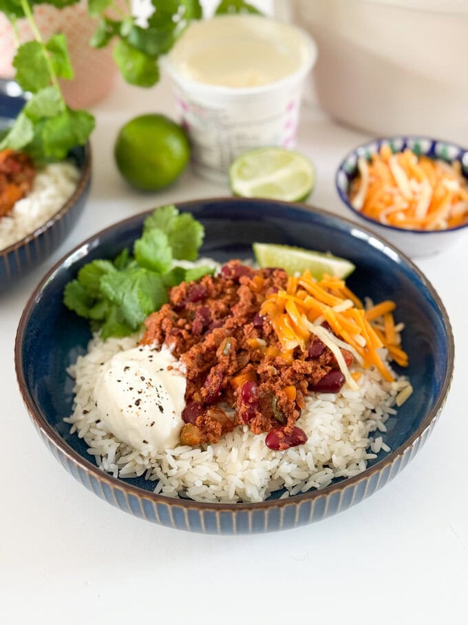 Served with white rice,grated cheese. And garnished with a slice of lime and a sprig of coriander. In a round dark blue bowl.